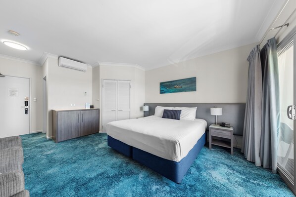 A hotel room with a large bed, a desk, a chair, and a painting on the wall. - Ocean Centre Hotel (Geraldton)