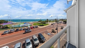 Vista da un balcone su un parcheggio con auto, una strada e una spiaggia sullo sfondo.