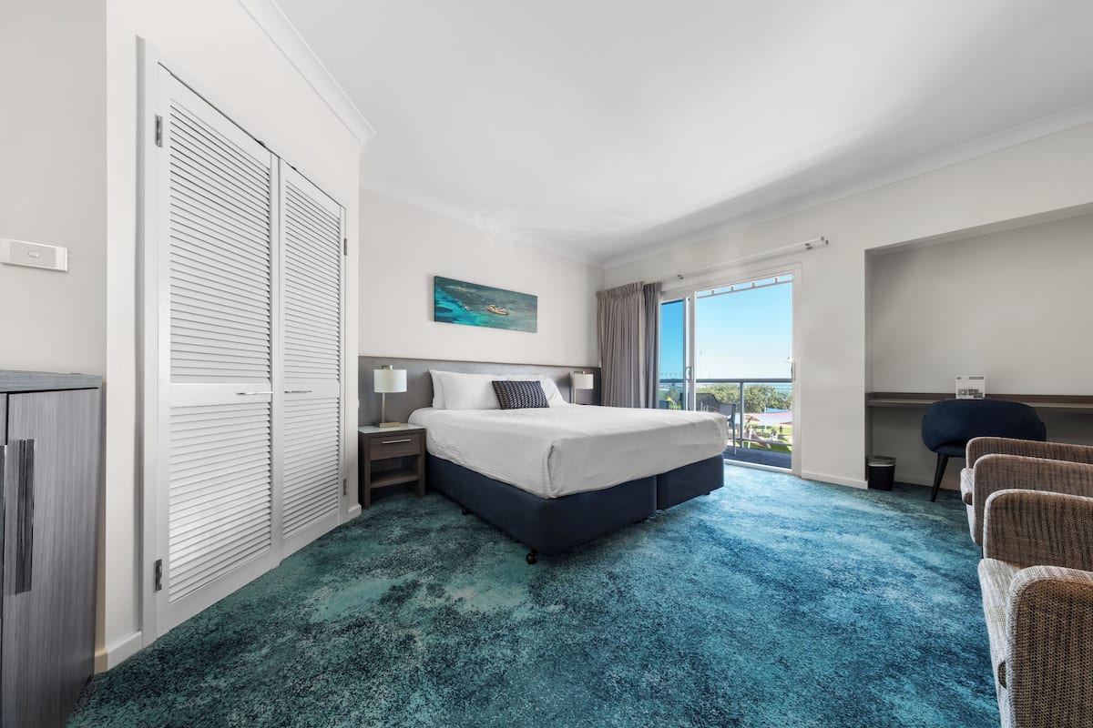 A hotel room with a large bed, a desk, a chair, and a view of the outdoors.