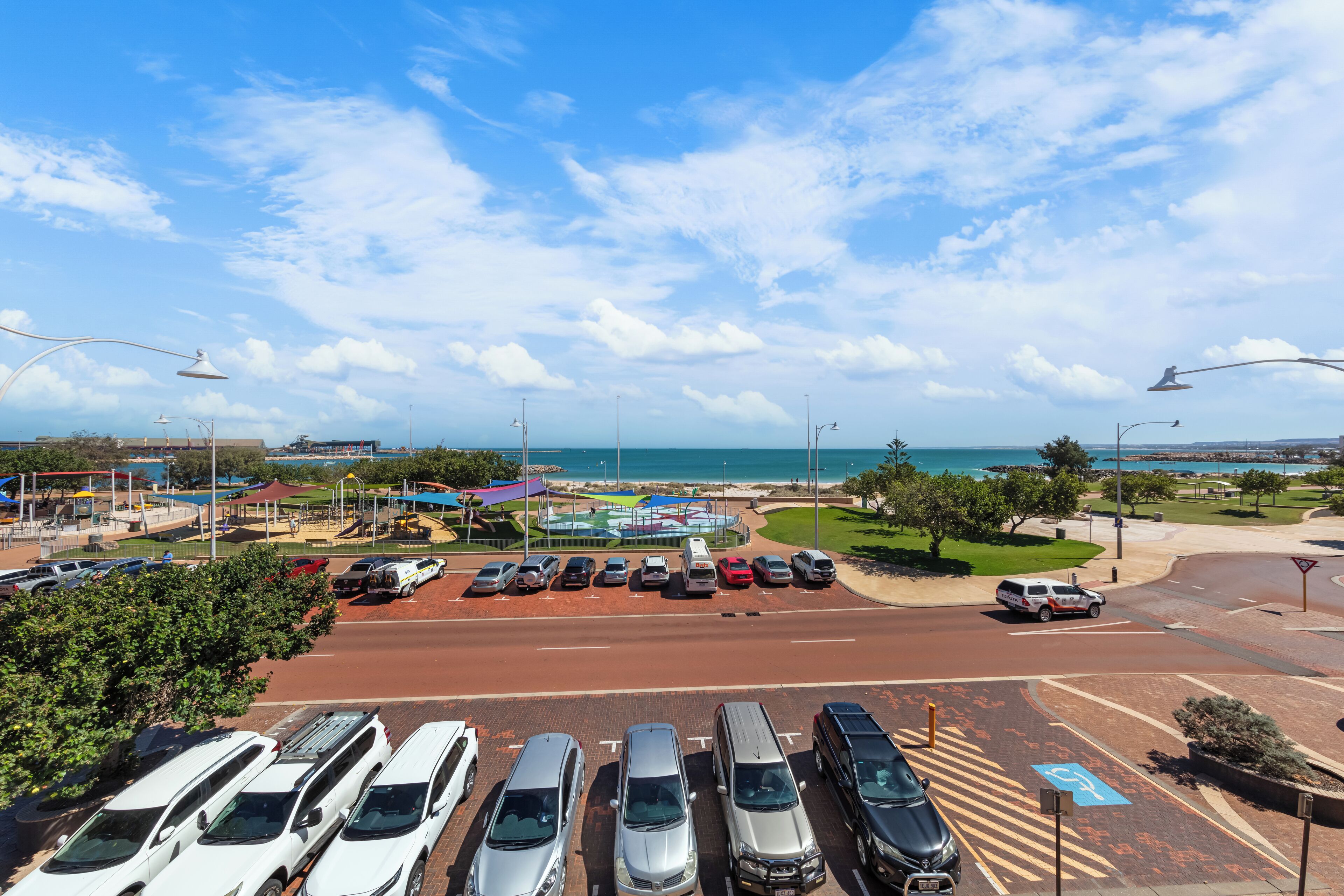 A parking lot with various vehicles, a road leading to a beach, and a clear sky.