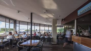 Un restaurante espacioso con amplios ventanales que ofrecen vistas al exterior. Hay varias mesas y sillas dispuestas para comer.