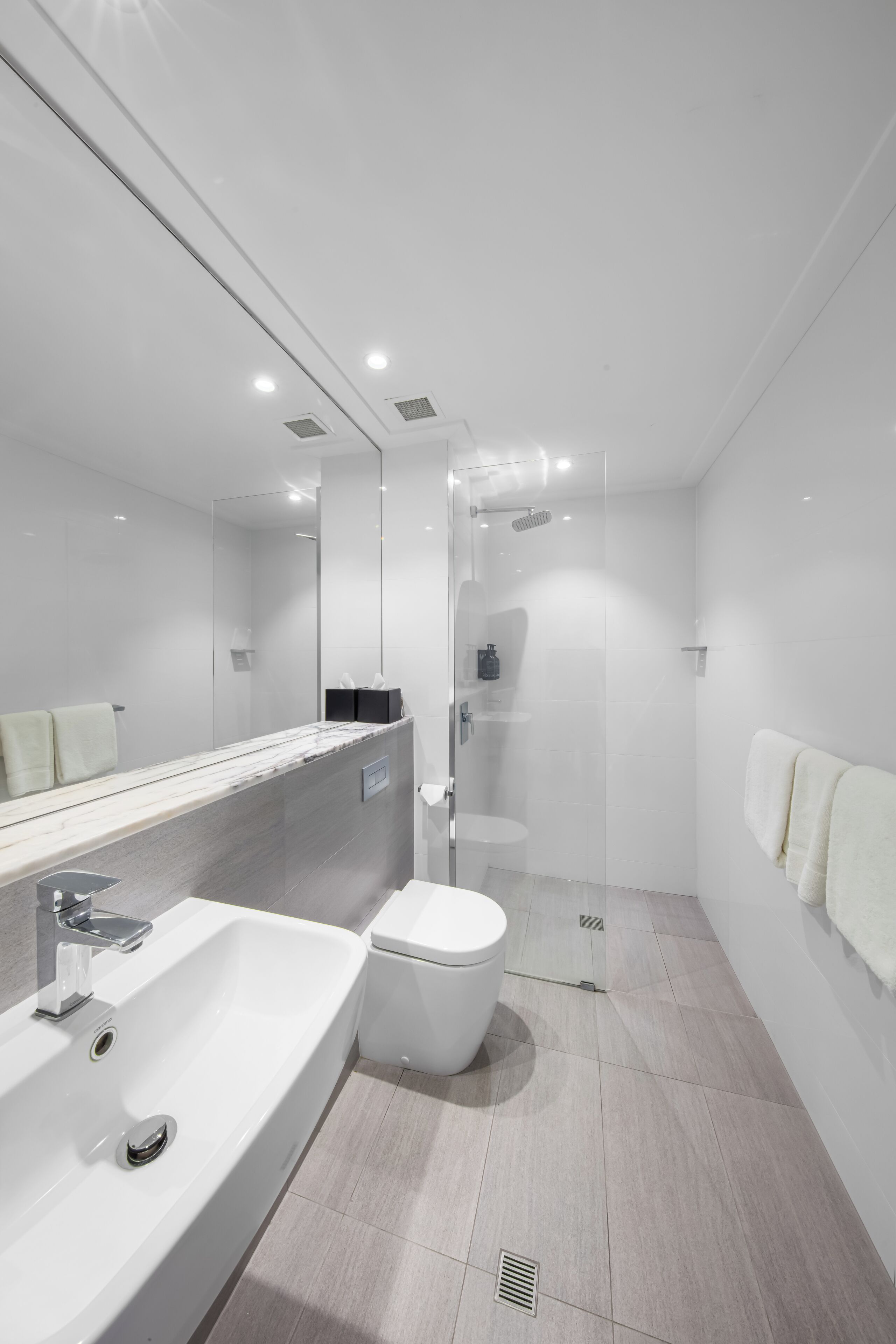 A modern bathroom with a large mirror, a sink, a toilet, and a shower area.