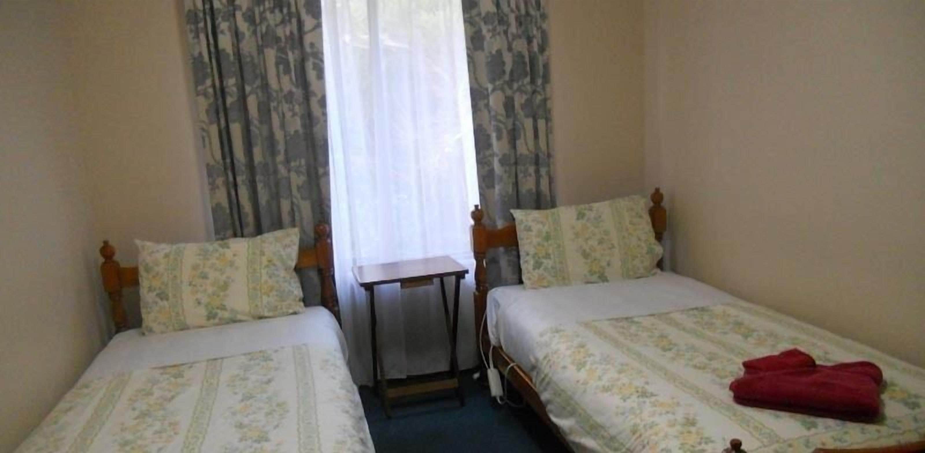 A room with two single beds, a small table, and a window with curtains.
