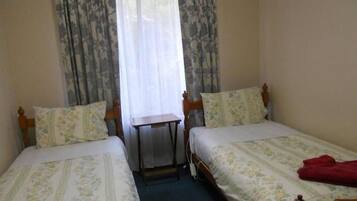 A room with two single beds, a small table, and a window with curtains.