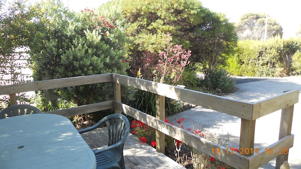 Una terraza de madera con una mesa y sillas, rodeada de exuberante follaje y plantas en flor.