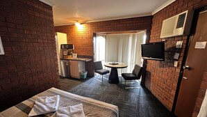 Une chambre d’hôtel comprenant un lit, une petite kitchenette, un coin repas avec une table et des chaises, et un téléviseur fixé au mur.
