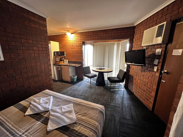 Une chambre d’hôtel comprenant un lit, une petite kitchenette, un coin repas avec une table et des chaises, et un téléviseur fixé au mur.