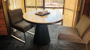 Une pièce avec une table ronde, deux chaises et une vue à travers des stores verticaux.