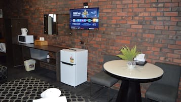 Hotellihuone, jossa on tiiliseinä, seinälle asennettu taulutelevisio minibaarin yläpuolella, pieni jääkaappi, pyöreä pöytä maljakolla ja kaksi tuolia.