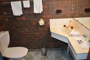 A bathroom with a toilet, a sink, and a mirror. There are towels hanging on a rack and a trash can.