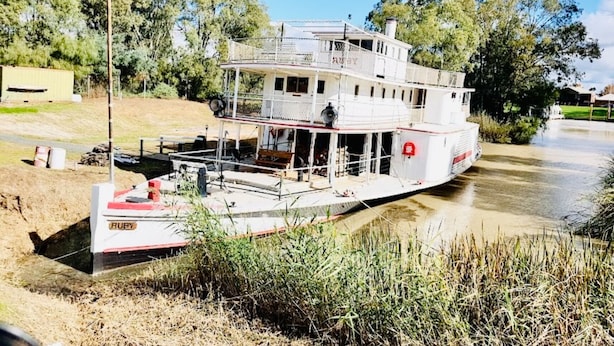 Un bateau à vapeur blanc était amarré sur la rive d’une rivière. Il était doté d’un pont couvert et d’une petite structure abritant une cabine.