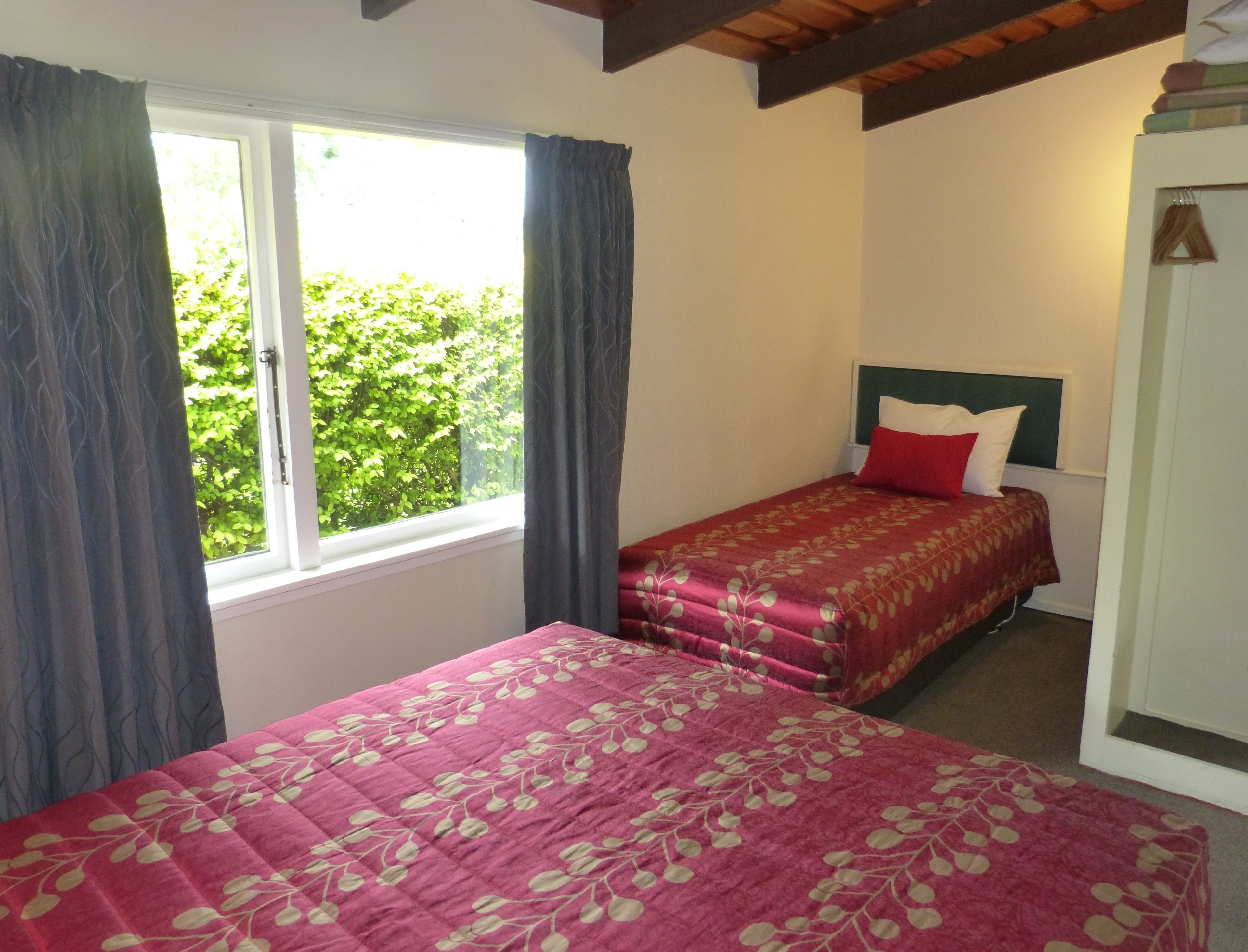 A bedroom with two beds, a window with curtains, a headboard, and a door.