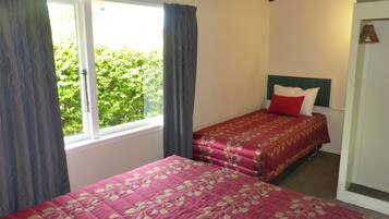 A bedroom with two beds, a window with curtains, a headboard, and a door.
