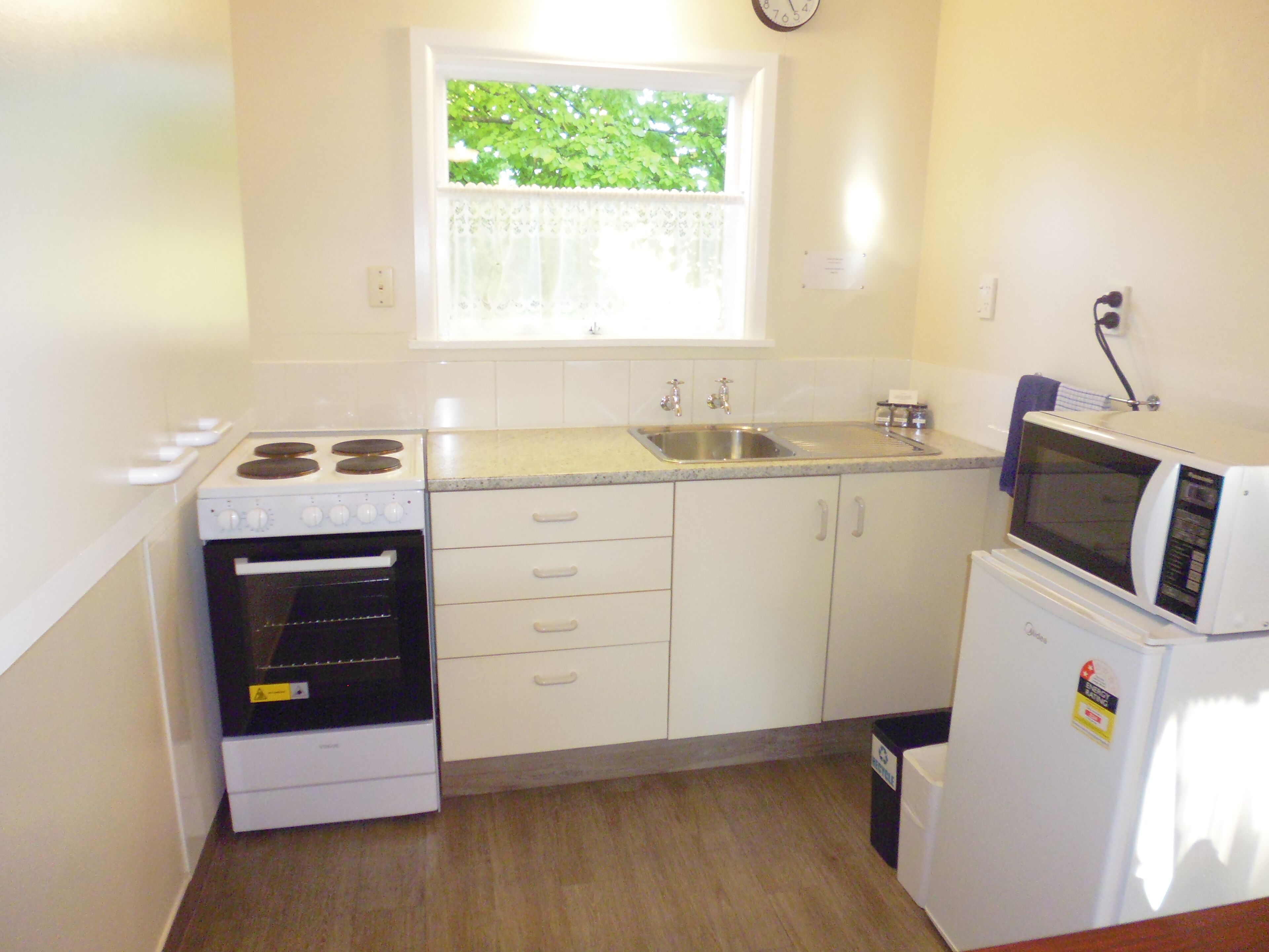 Une cuisine de taille réduite avec des meubles blancs, une cuisinière, un évier et un four à micro-ondes.