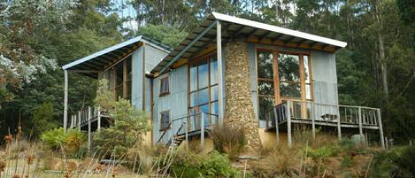 Una casa de dos pisos con fachada de piedra, ventanas grandes y un balcón.