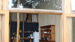 Un comedor de madera abierto con una mesa y sillas, una zona de cocina con armarios y electrodomésticos, y vistas a árboles a través del ventanal.