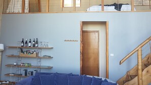 Una habitación de dos pisos con zona de altillo, vigas de madera, escalera de madera y sofá.