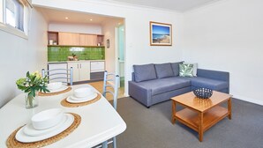 Un espacio habitable compacto con kitchenette, una zona de comedor con mesa para dos y una sala de estar con sofá y mesa de centro.