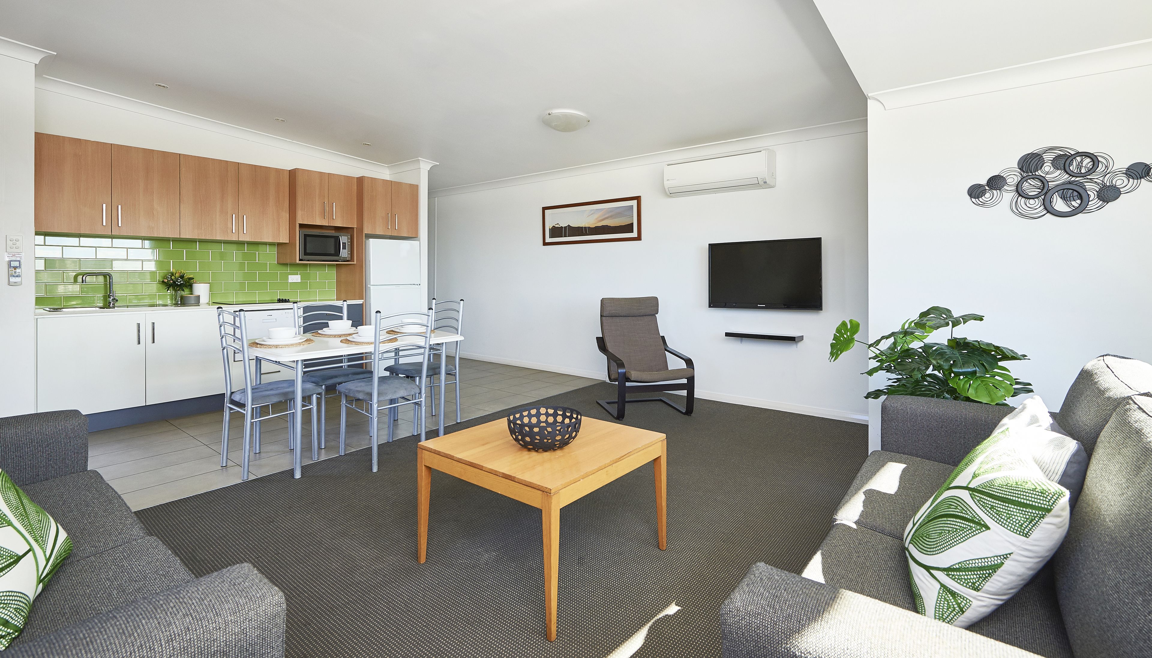 Un apartamento moderno con cocina, comedor y sala de estar. Cuenta con una mesa de comedor con sillas, un sofá, un televisor y una planta.