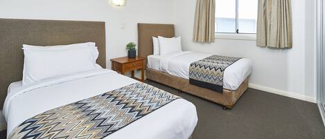 A hotel room with two beds, a nightstand, a potted plant, and a window with curtains.