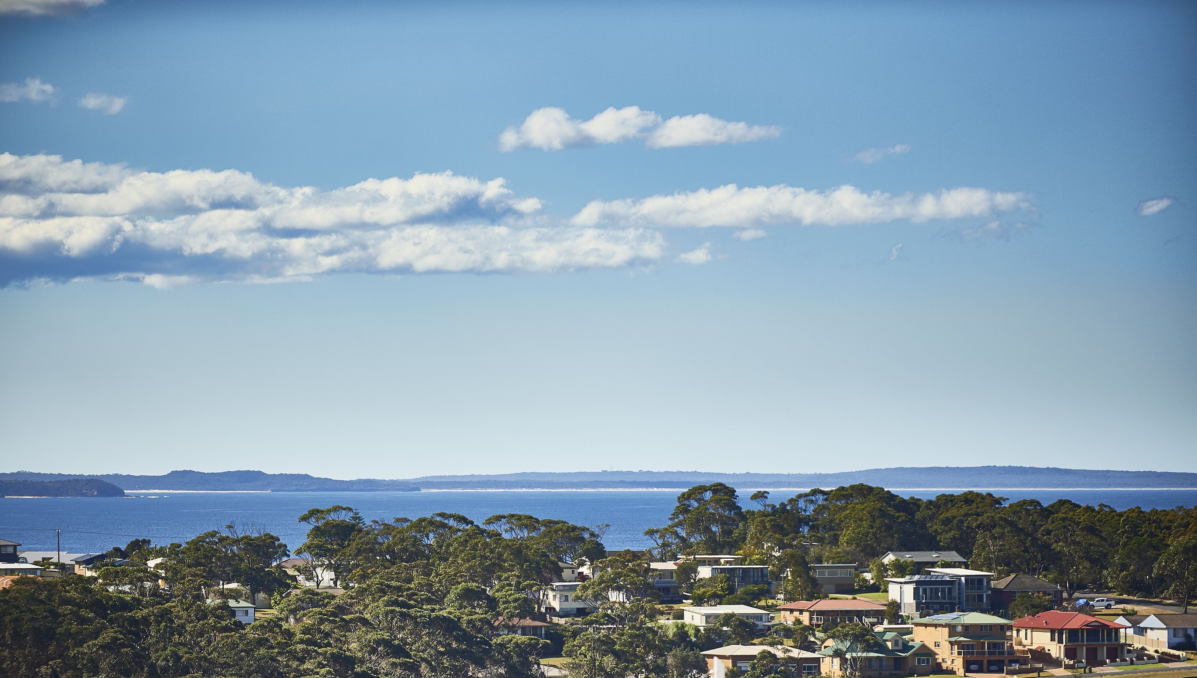 A coastal residential area with houses, trees, and a view of the sea.
