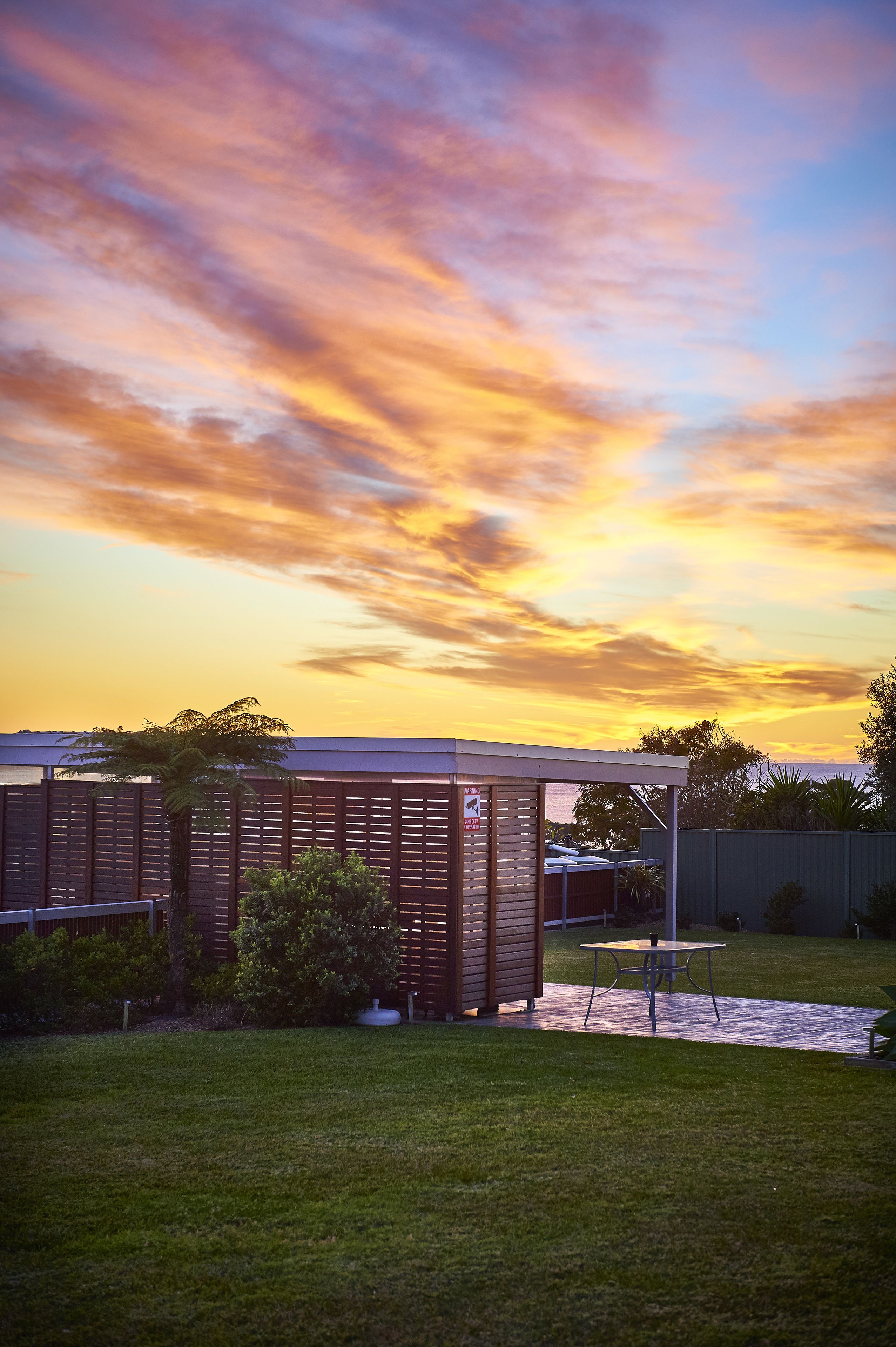 A modern building with a flat roof, surrounded by a well-maintained lawn and a wooden fence.