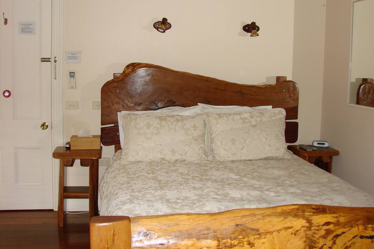 A bedroom with a wooden headboard, two bedside tables, a bed with a patterned bedspread, and a nightstand with a clock.