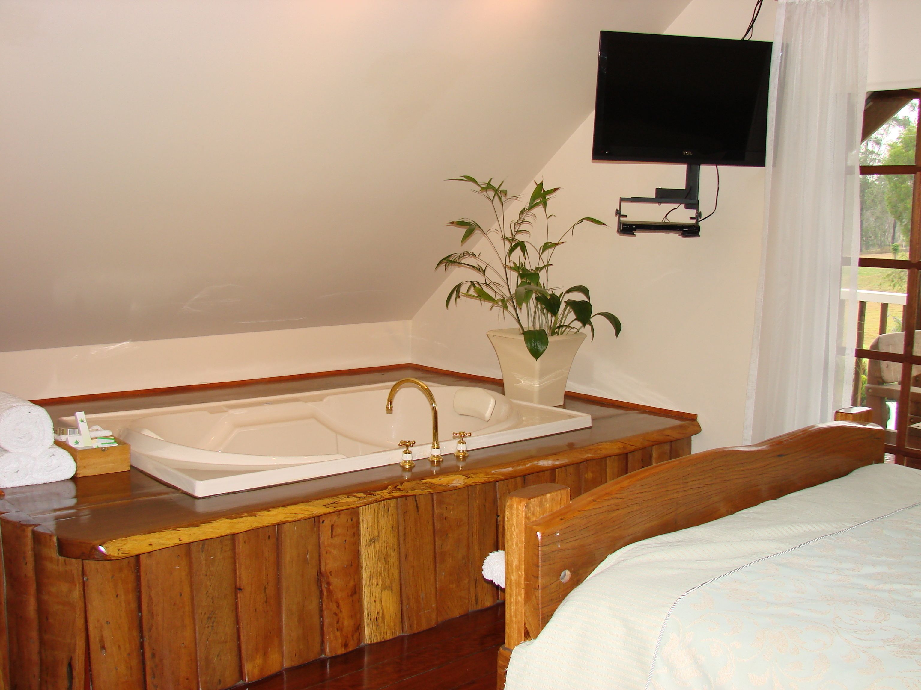 A bathroom with a wooden vanity, a bathtub, a potted plant, and a mounted TV.