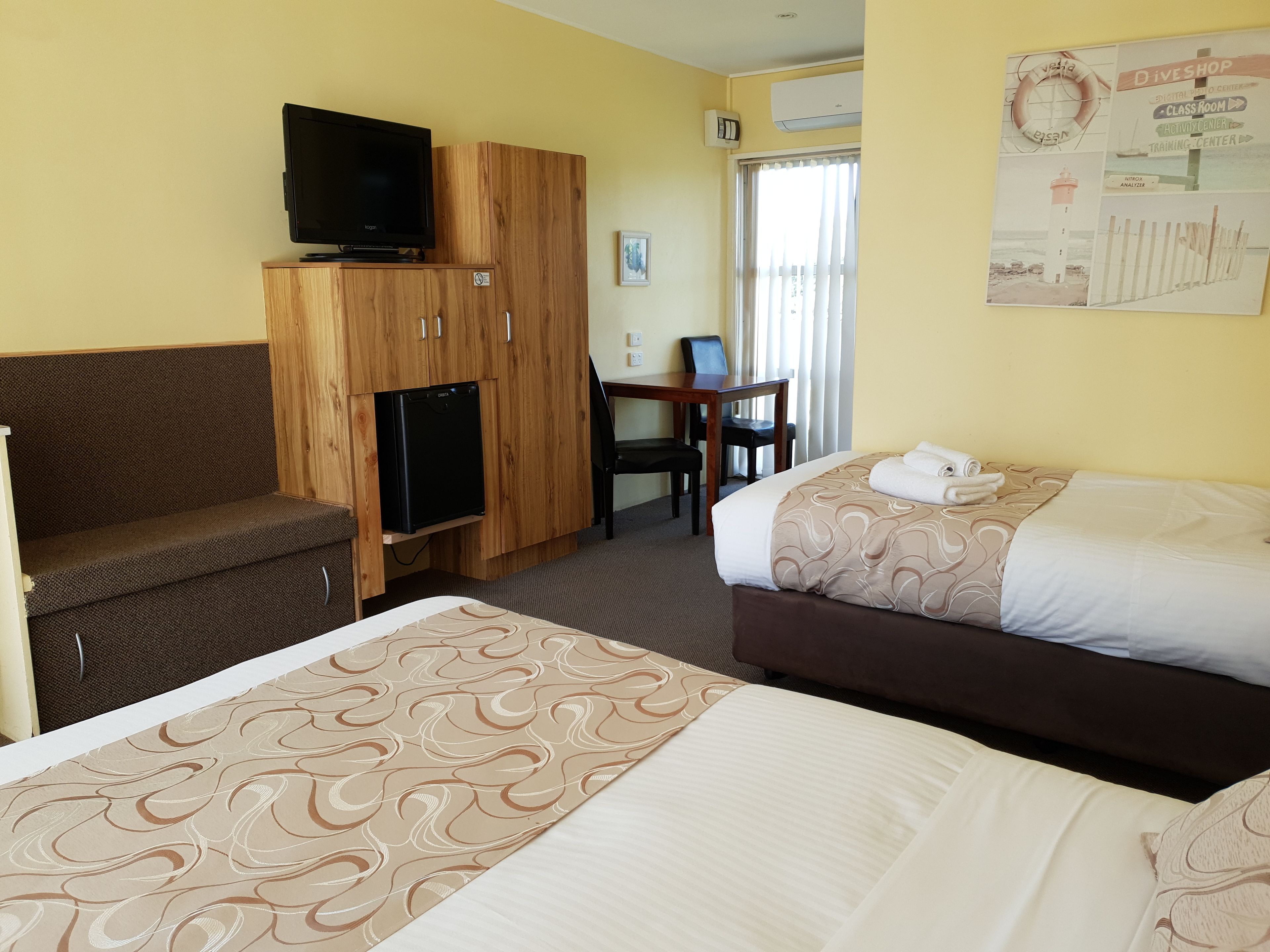Camera d'albergo con due letti, una scrivania, una sedia, una televisione e un frigorifero.