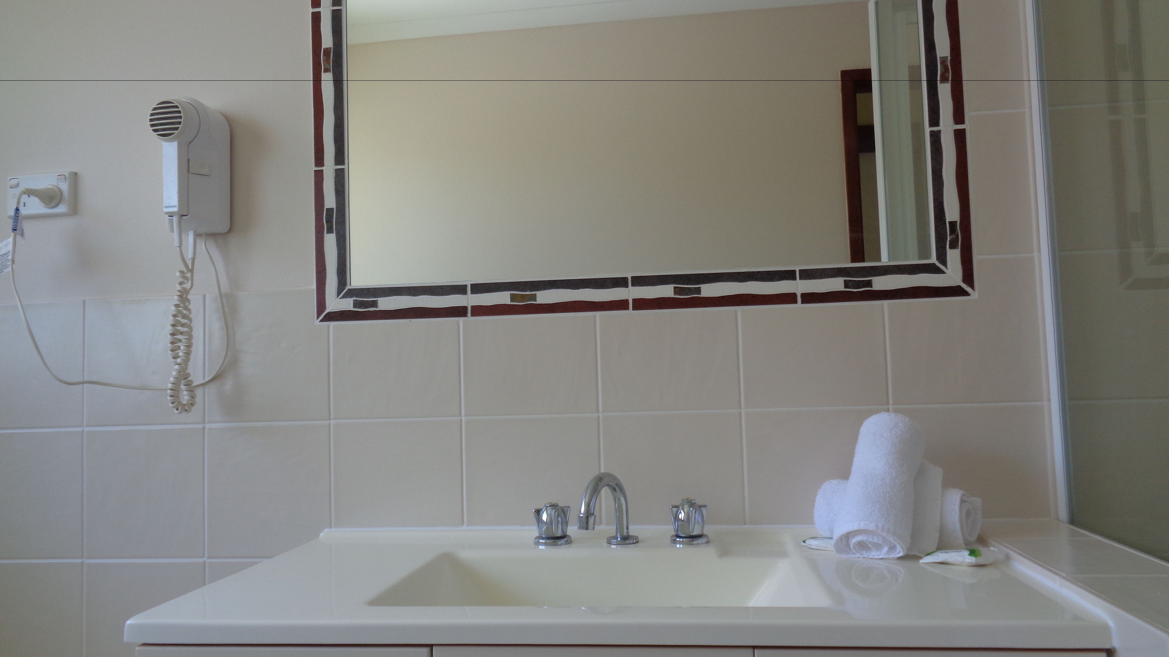 A bathroom with a white sink, a mirror, and a hairdryer on the wall.
