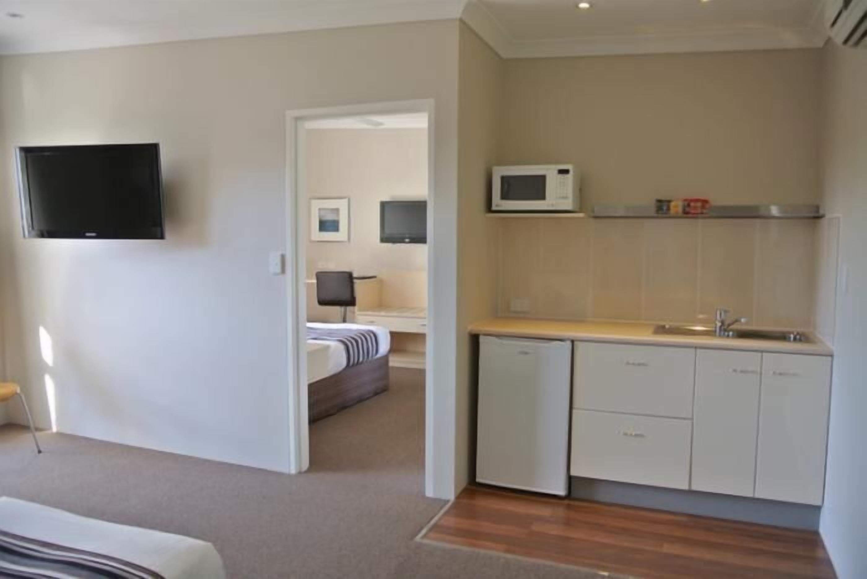 A compact hotel room with a kitchenette, a flat-screen TV, a bed, and a small seating area.