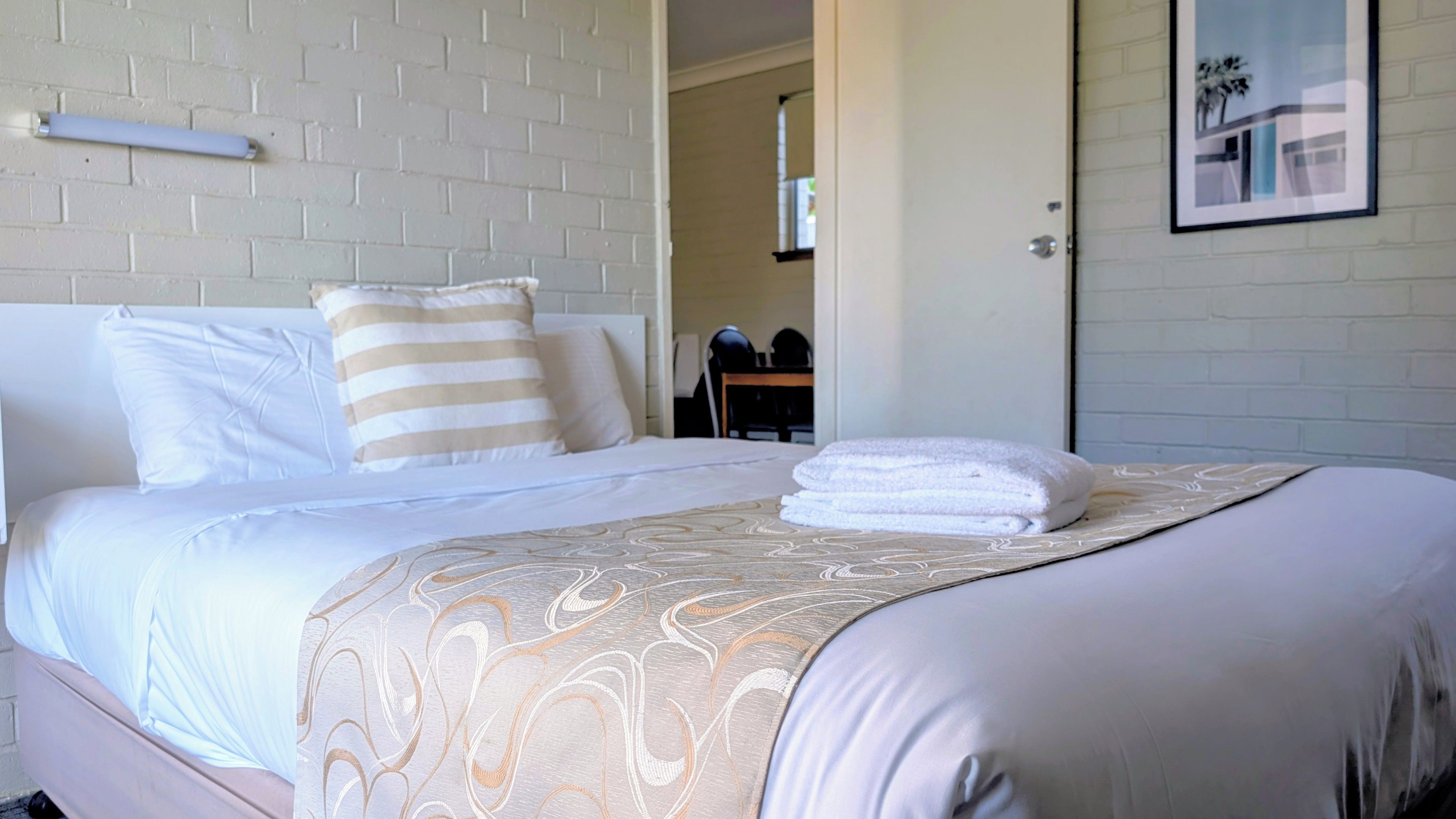 A neatly made bed with a patterned bedspread, a striped pillow, and a folded towel on the bed.