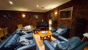 A cozy living room with leather sofas, a coffee table, a TV, and a wine rack. - Moon River Motor Inn (Kempsey)