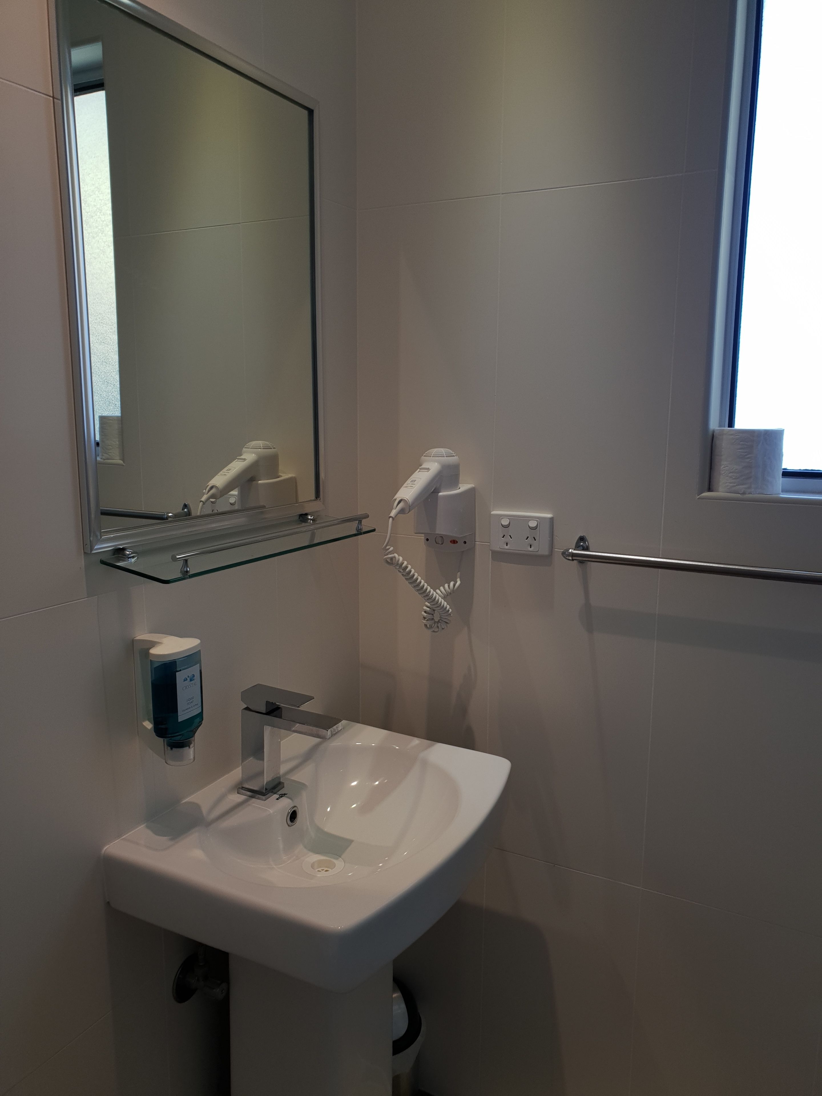 Une salle de bain moderne avec un lavabo blanc, un sèche-mains, un miroir et une fenêtre.