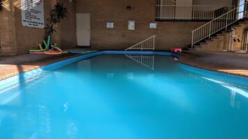Swimmers can enjoy the pool surrounded by a brick wall and stairs leading to a balcony.