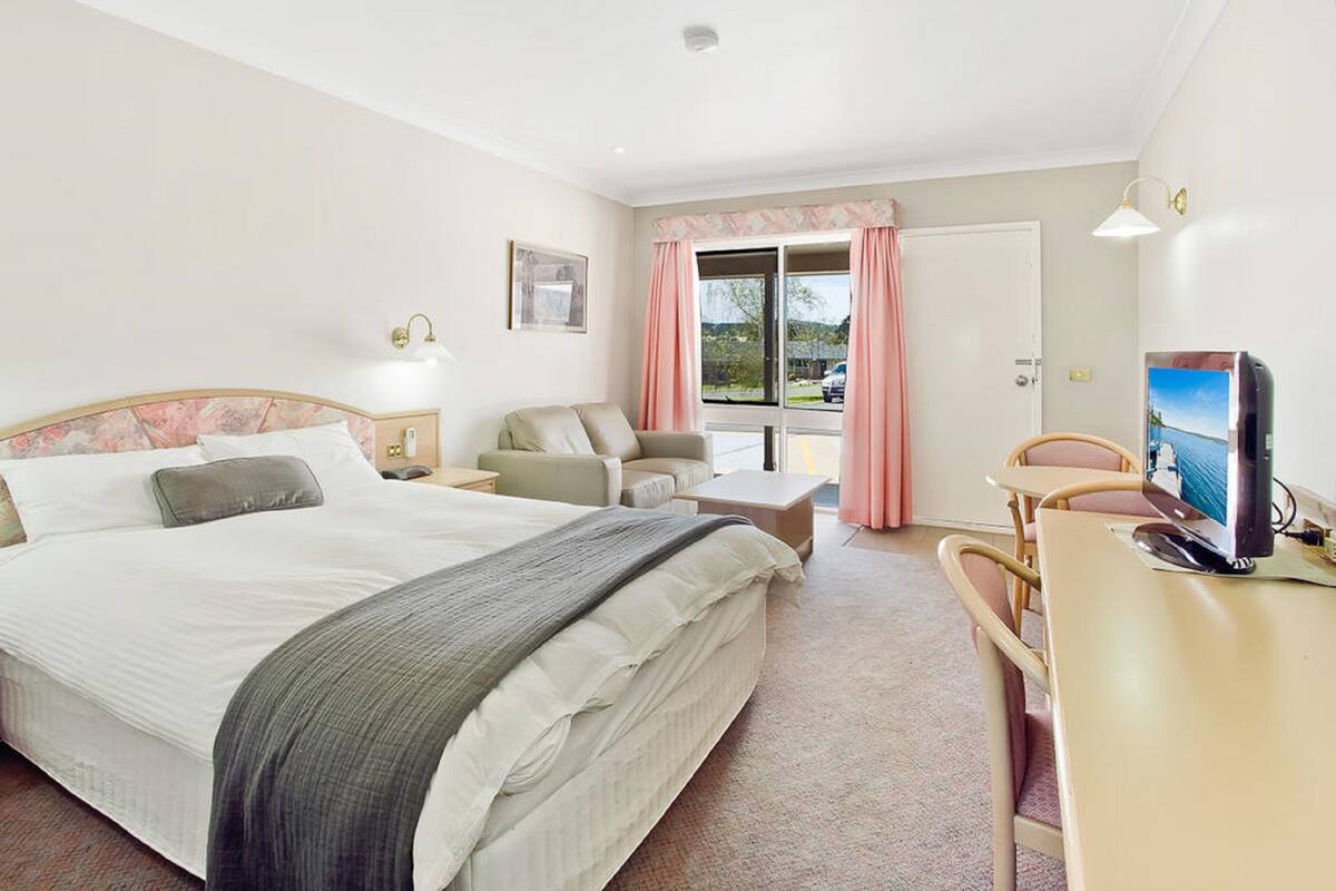 A hotel room with a bed, a desk with a computer, a chair, and a window with curtains.