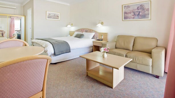 Habitación de hotel con cama, sofá, mesa y sillón. Seis mesitas de noche, dos con lámparas y un espejo.
