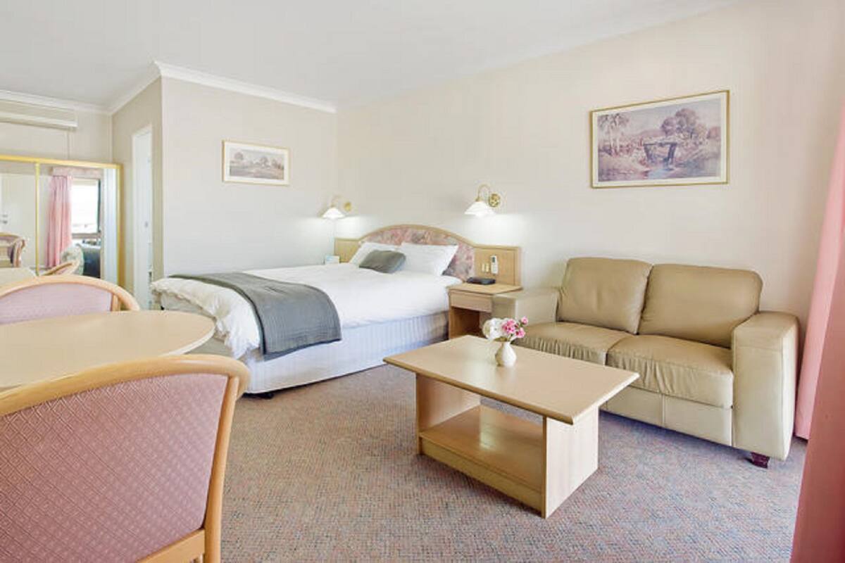 A hotel room with a bed, a sofa, a table, and a chair. There are two bedside tables with lamps and a mirror.