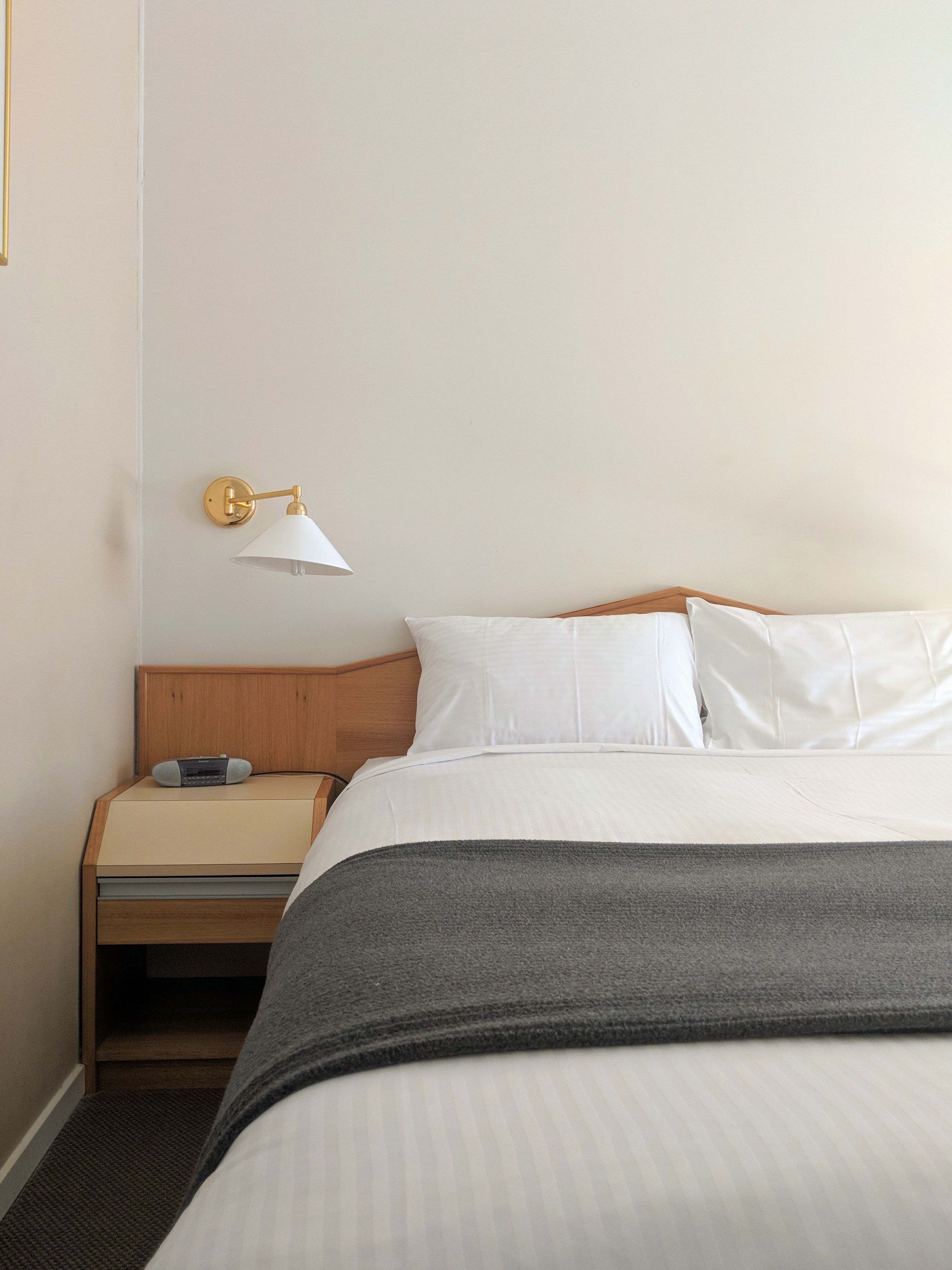 Una habitación de hotel con una cama, una mesita de noche con lámpara y un radio.
