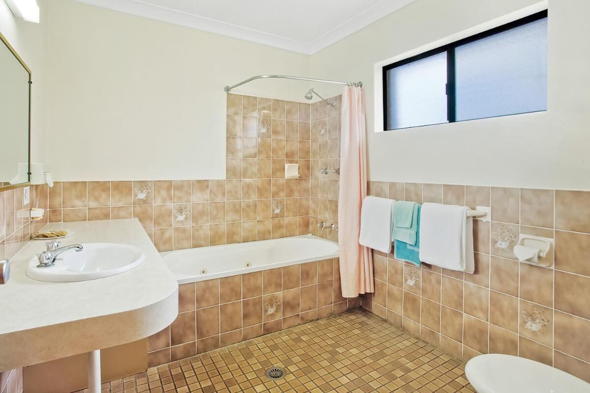 A bathroom with a sink, bathtub, and toilet. There is a window above the toilet and a shower curtain.