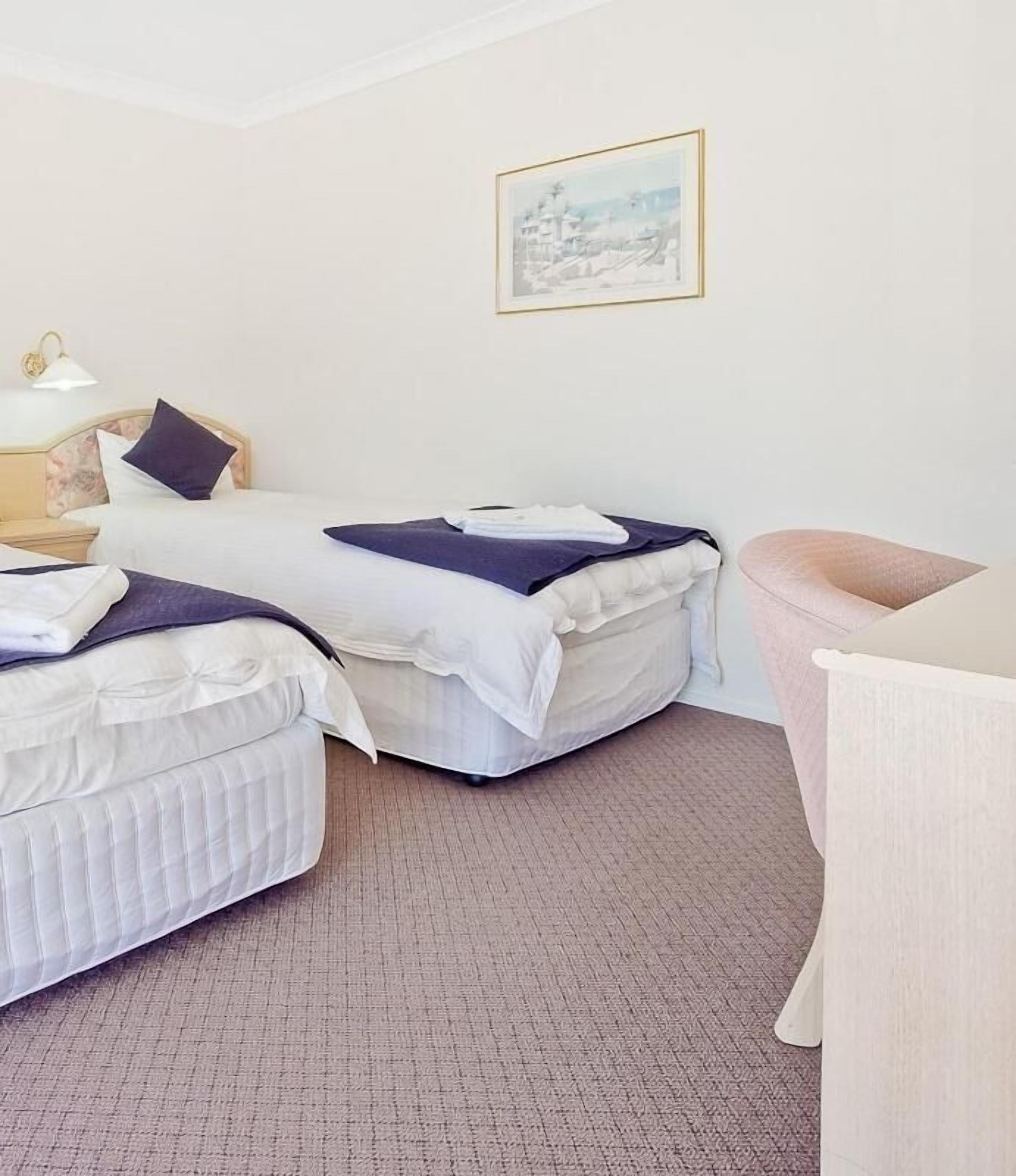 Quarto de hotel com duas camas, uma escrivaninha e uma cadeira.