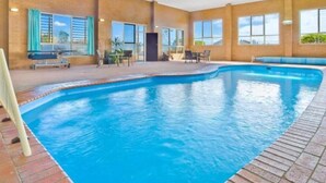 Una piscina interior con agua azul cristalina, rodeada de paredes de ladrillo y grandes ventanales.