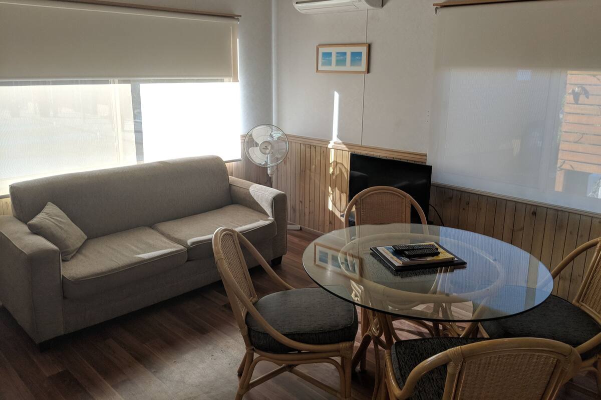 A living room with a sofa, a glass table with chairs, a fan, and a TV.