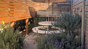 Una terraza de madera con un pérgola, un espacio de asientos circular y diversas plantas, incluyendo lavanda.