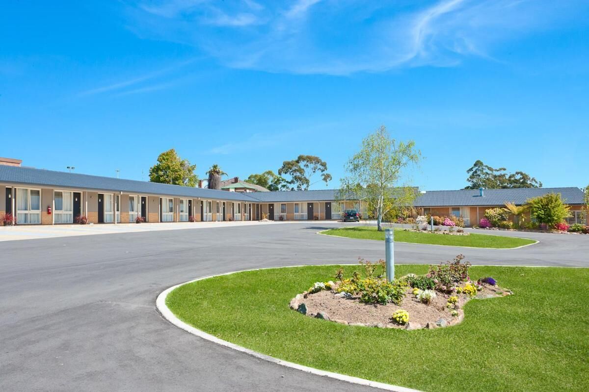 Un motel con un césped central, un estacionamiento y una hilera de habitaciones.