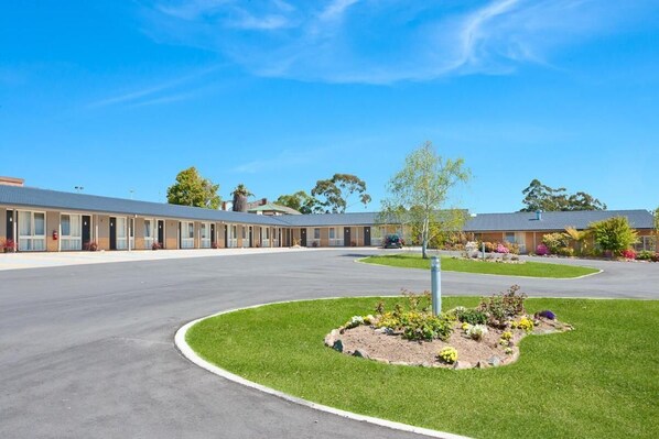 A motel with a central lawn area, a parking lot, and a row of rooms.