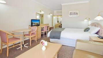 Habitación de hotel con una cama, un escritorio con silla, una mesita con un jarrón de flores y un televisor.
