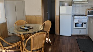 Una cocina compacta con una mesa de vidrio, sillas de mimbre y una estufa.