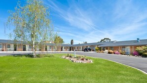 Un motel con una hilera de habitaciones, estacionamiento y césped bien cuidado.