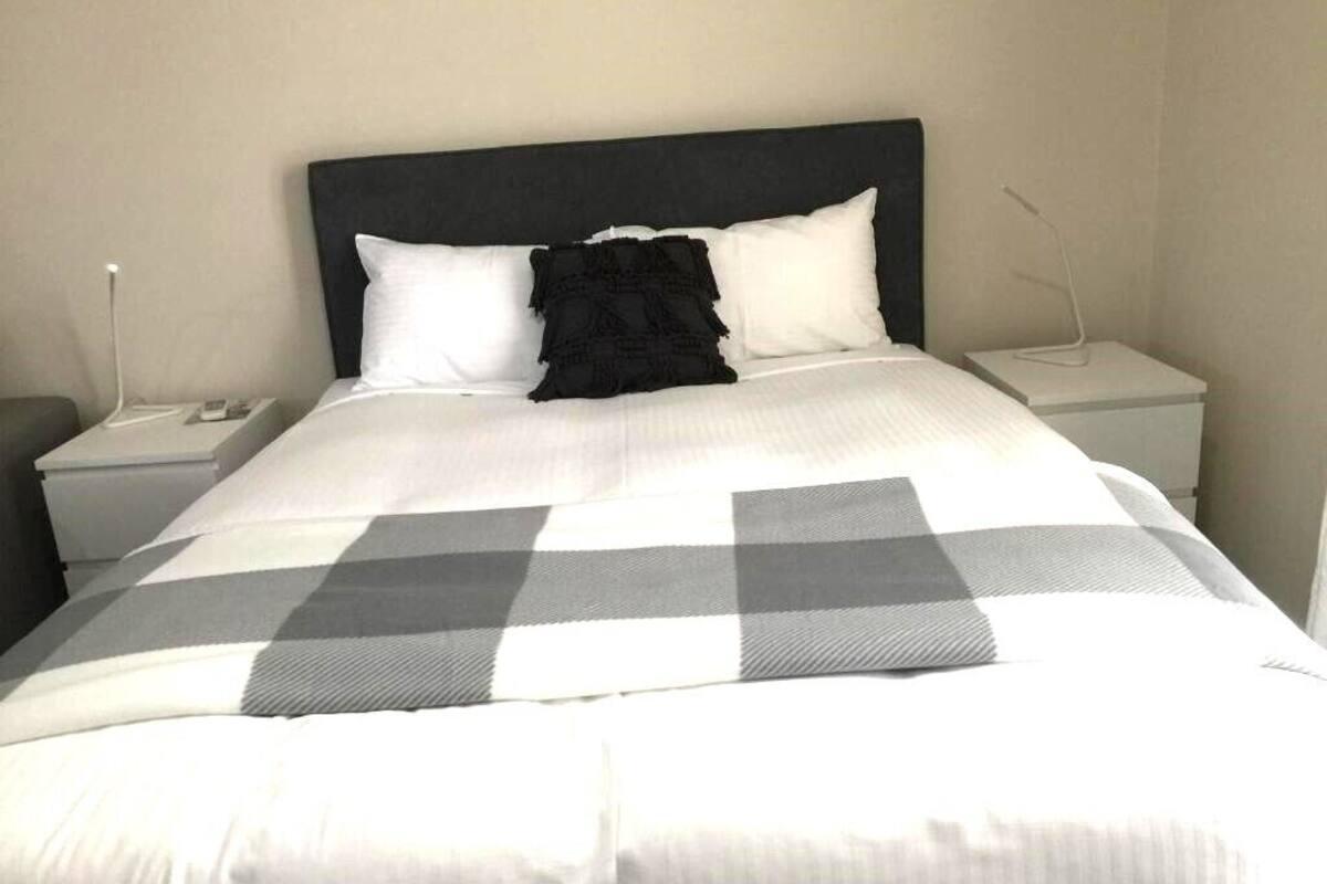A neatly made bed with a checkered bedspread, two white pillows, and a black decorative pillow.